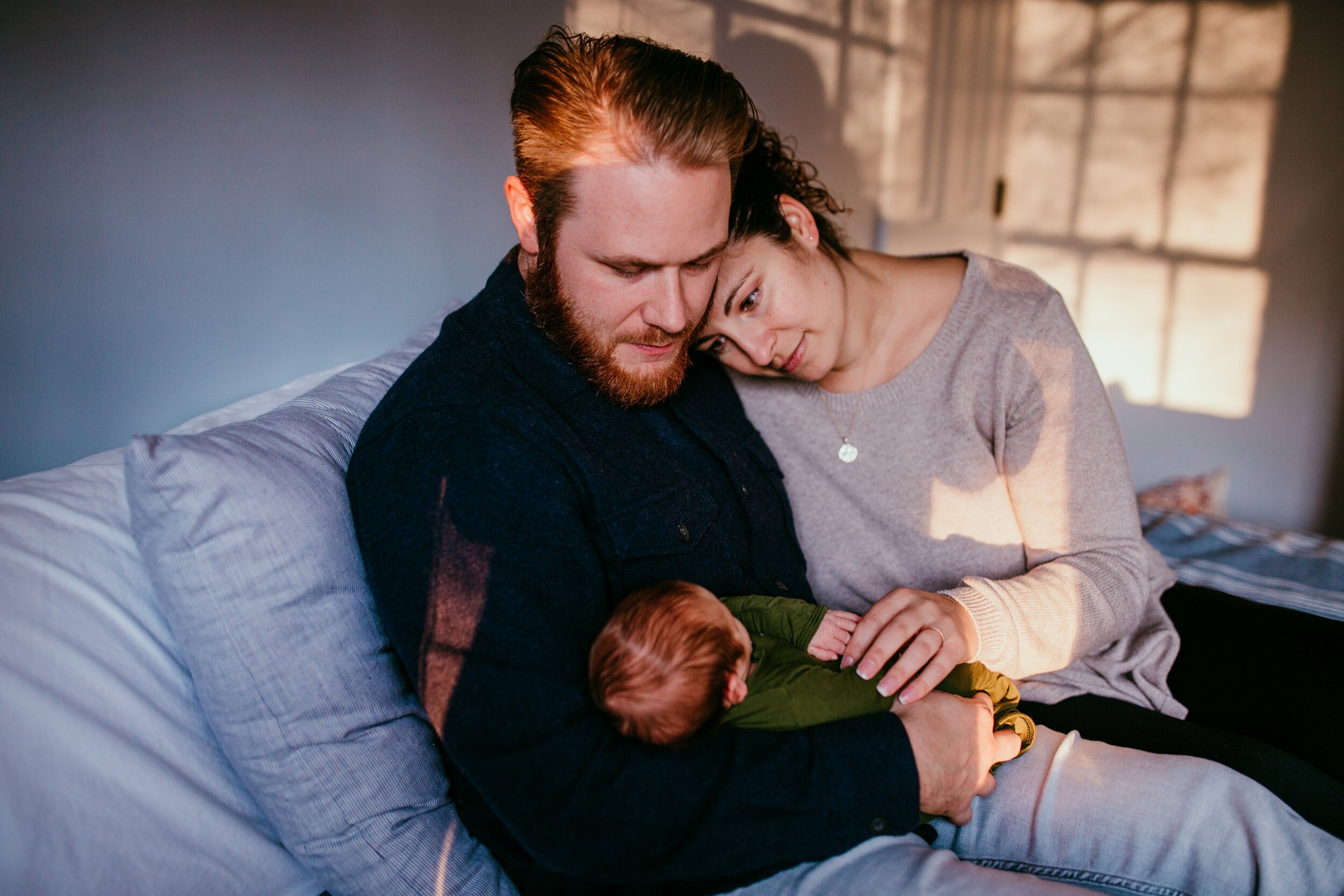 new parents look at baby with sunset light coming in through the window 