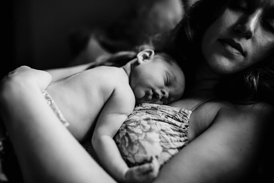 mother sleeps with newborn on her chest in black and white 