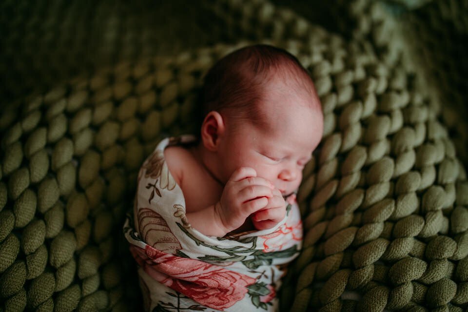 close up of newborn on green knit blanket with hands folded