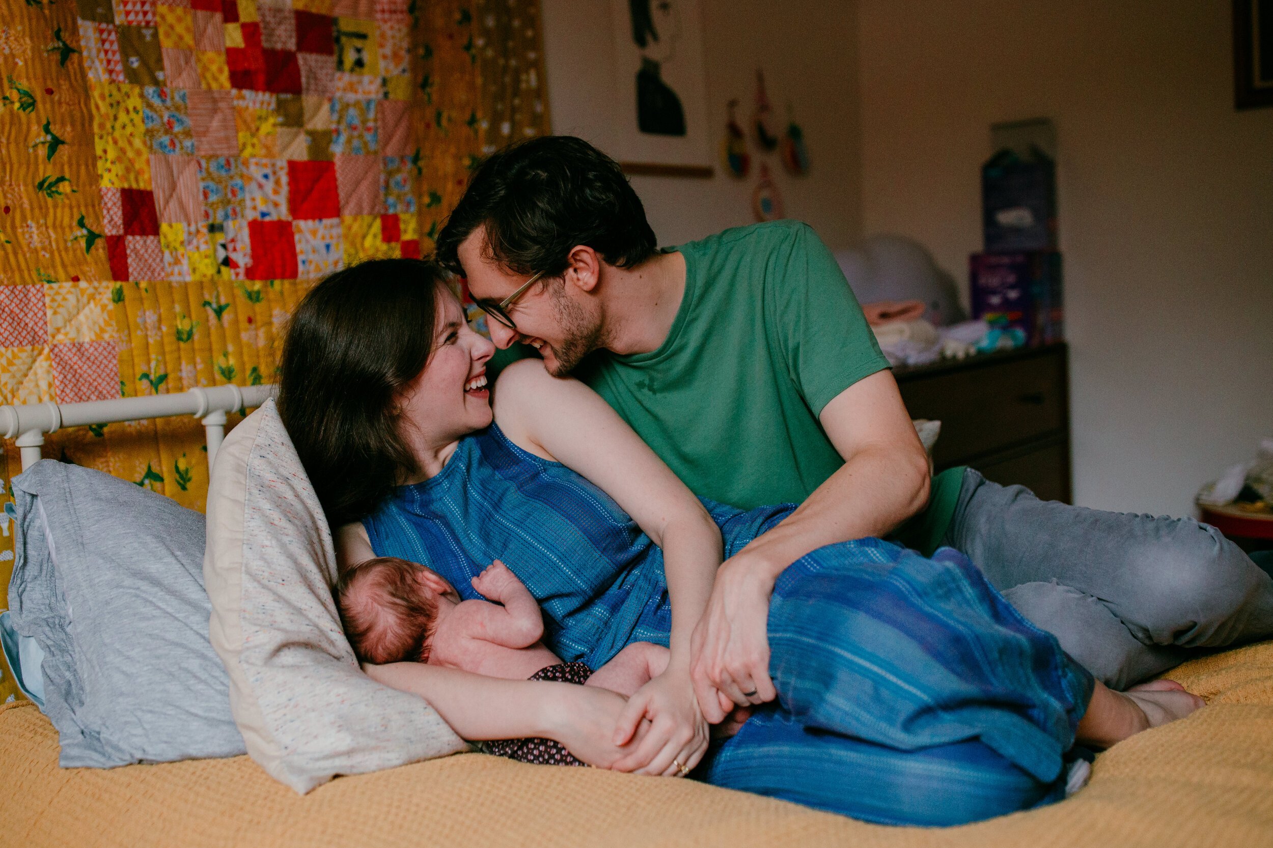 new parents snuggle together on yellow bed holding newborn