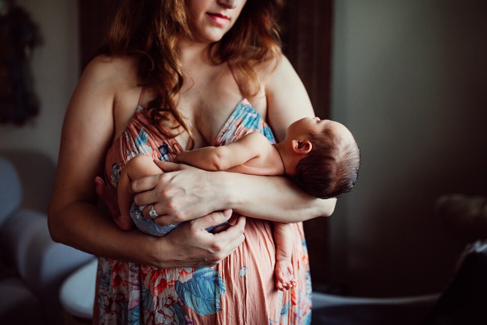 mother holds newborn in arms while wearing flowy floral dress