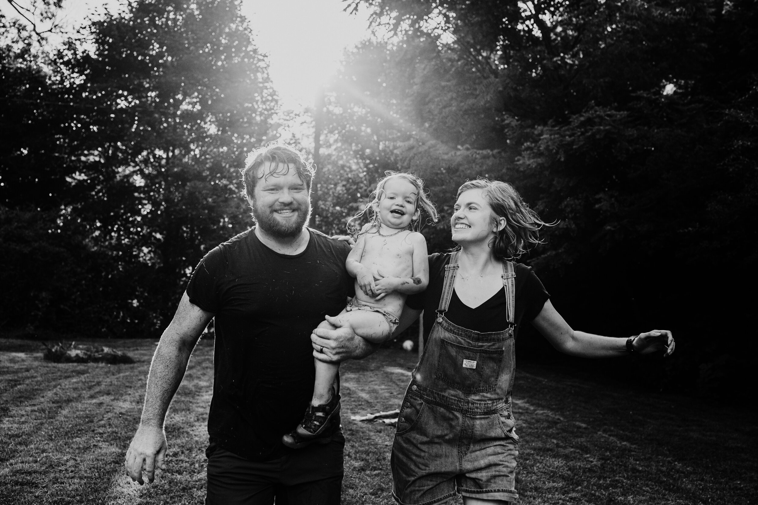 family of three laugh together running in their yard at sunset in black and white 