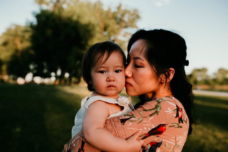 mother snuggles infant daughter at sunset close up on faces 