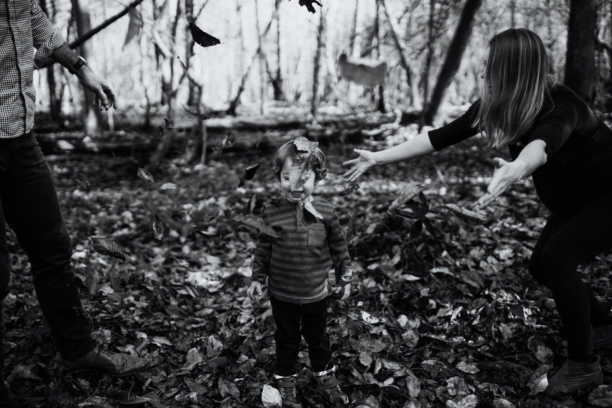 family plays in Fall leaves with toddler in black and white