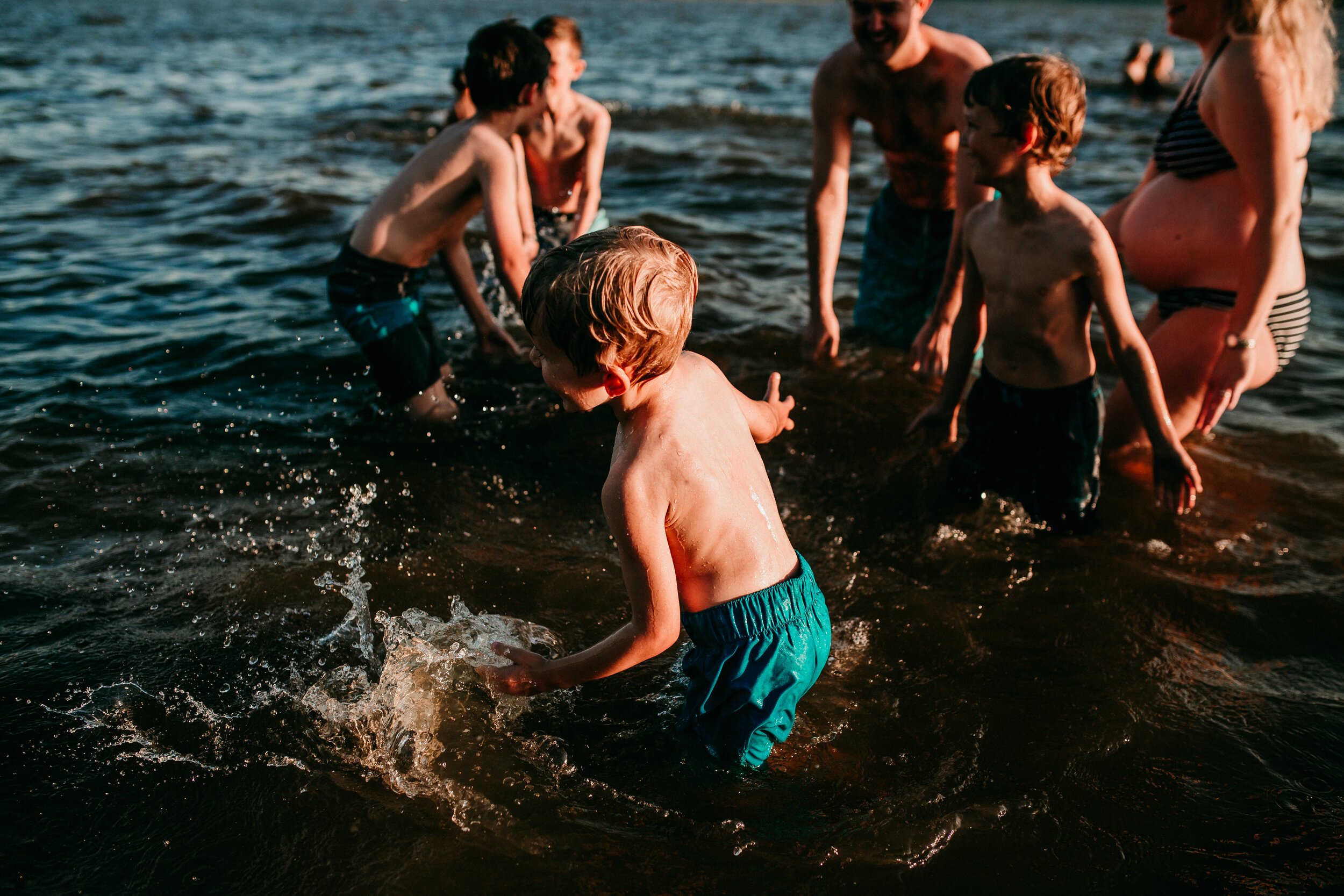 family of boys splash around in the lake at sunset in blue swim trunks