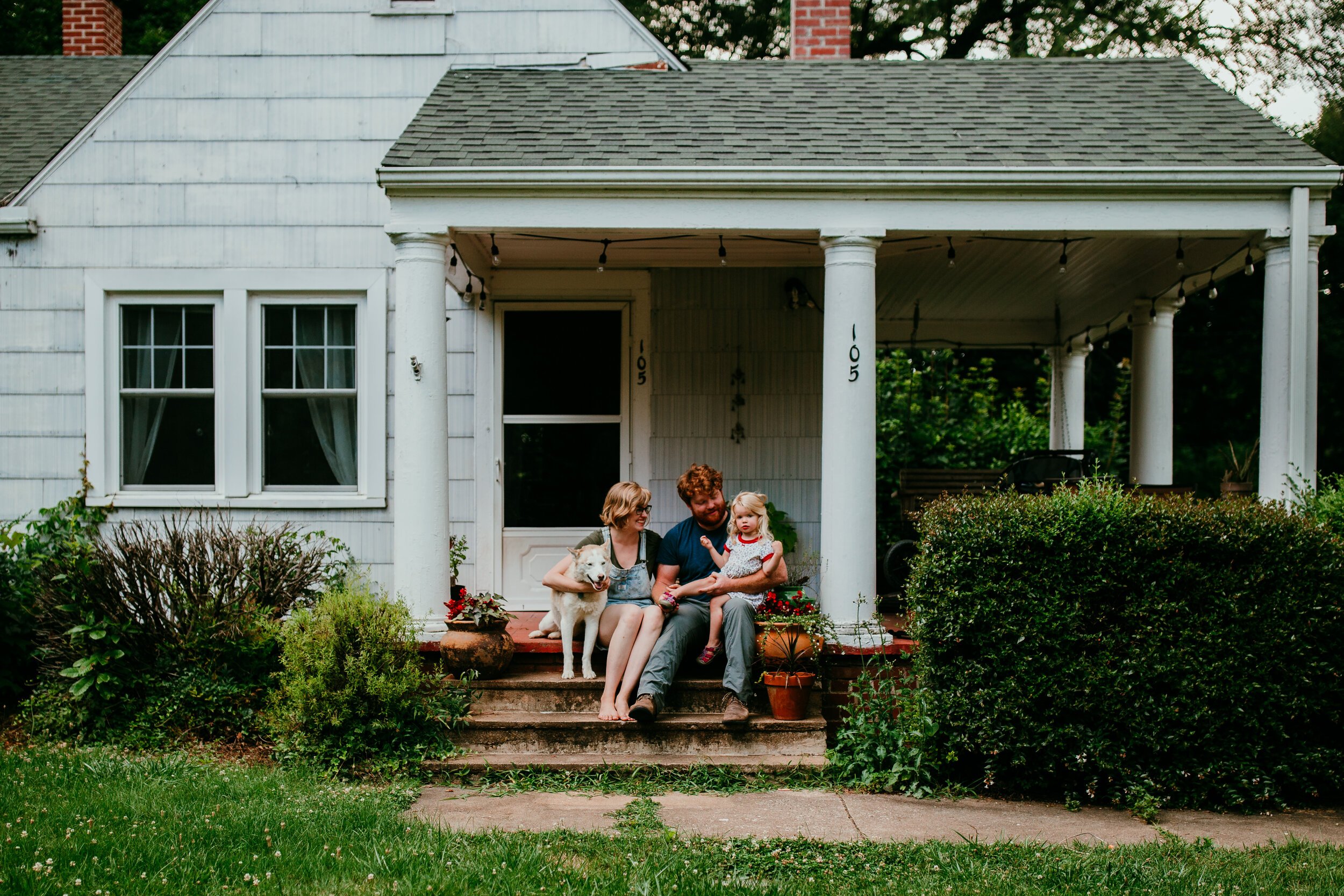 family of three sit together with husky dog on front porch of their craftsman bungalow