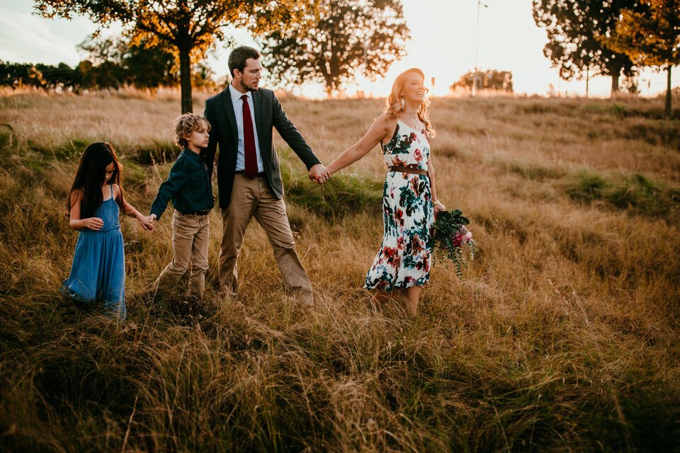 family of four walk together down a grassy hill at sunset holding hands
