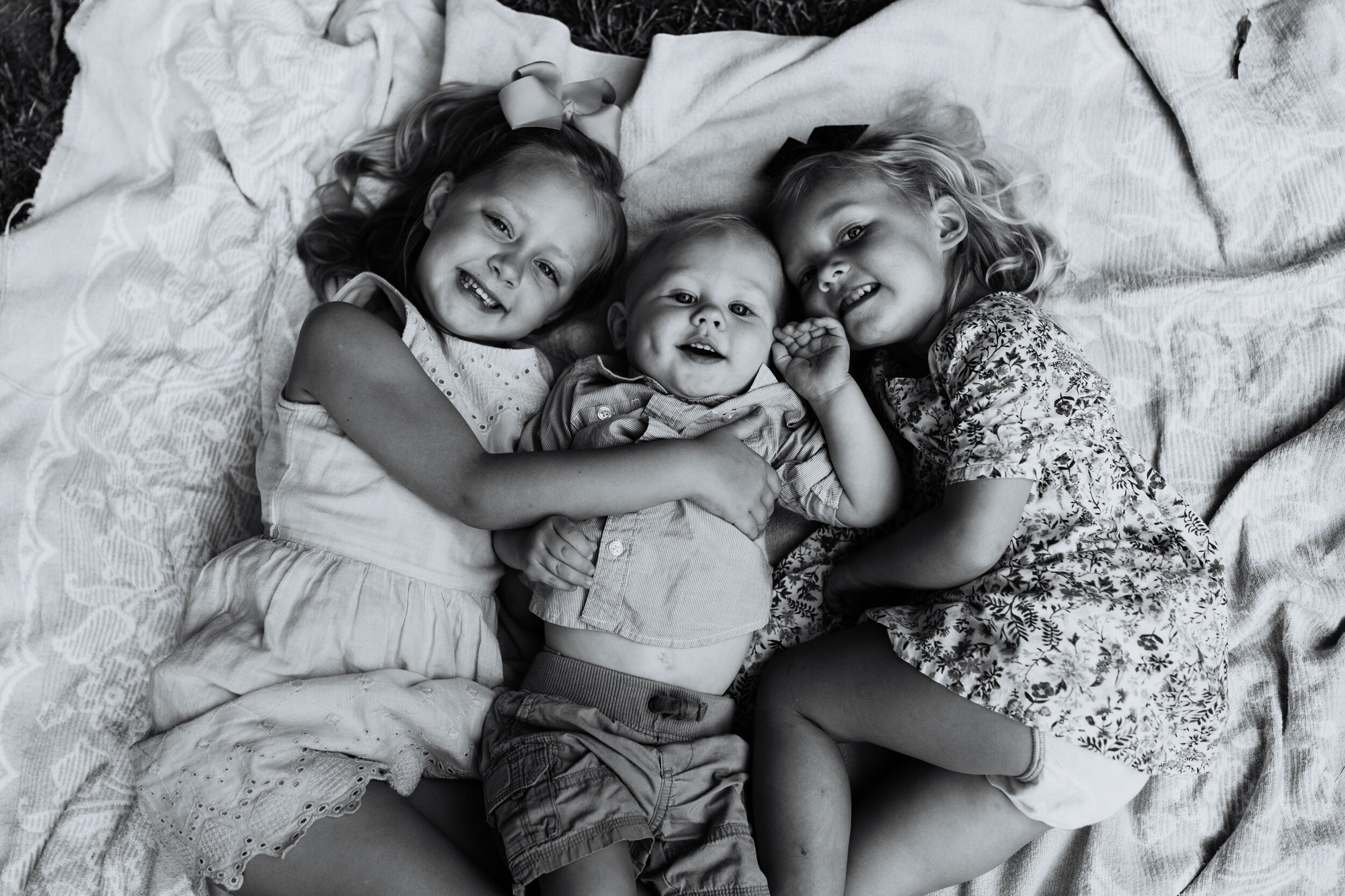 three siblings lay on blanket at park view from above while children smile black and white