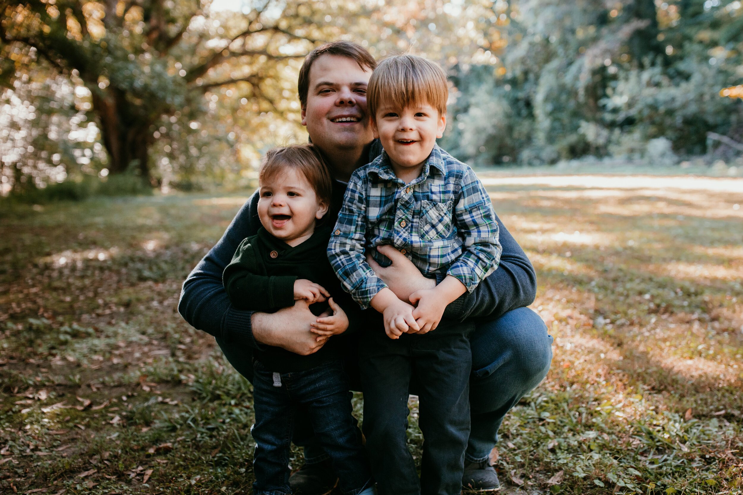 father kneels down beside two toddler sons smiling at camera