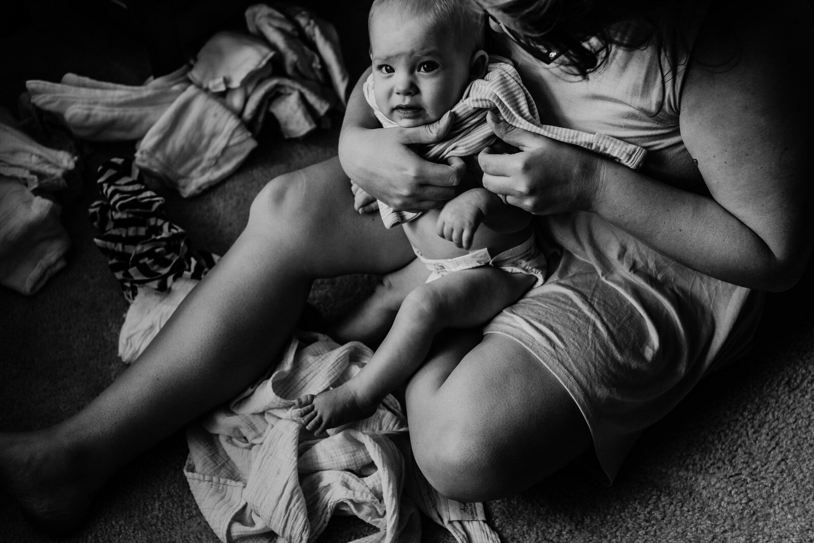 mother sits on floor dressing small child in black and white Documentary family photography