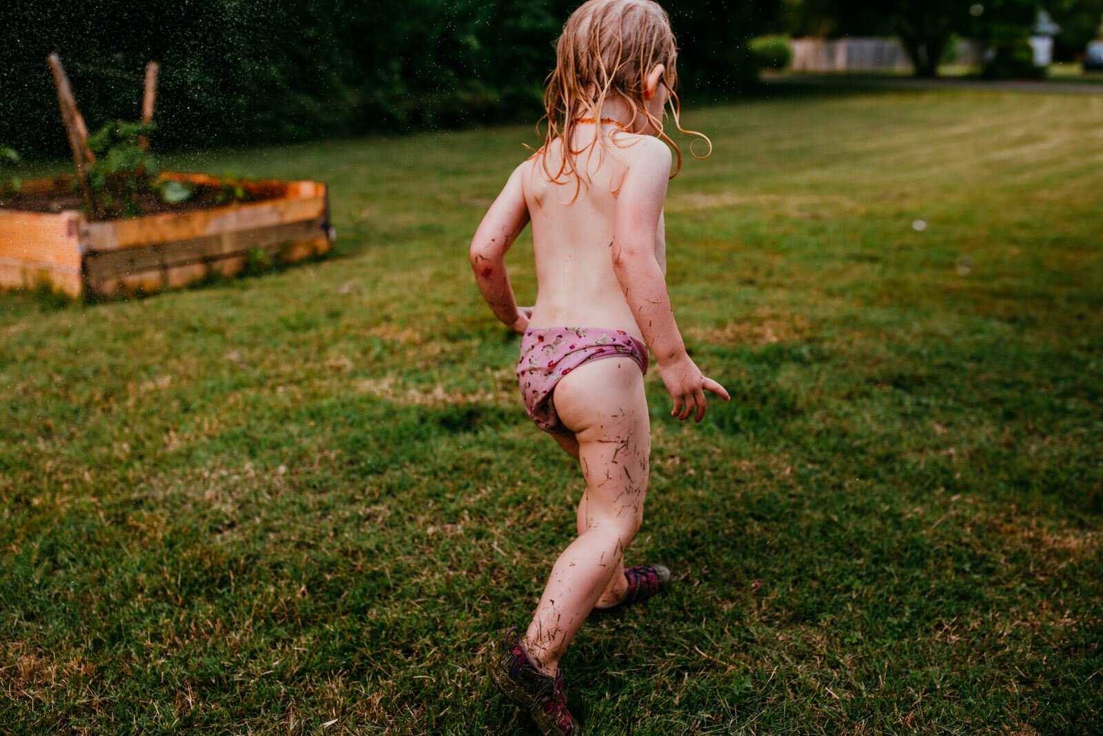 little girl walk in her garden soaking wet after playing with hose