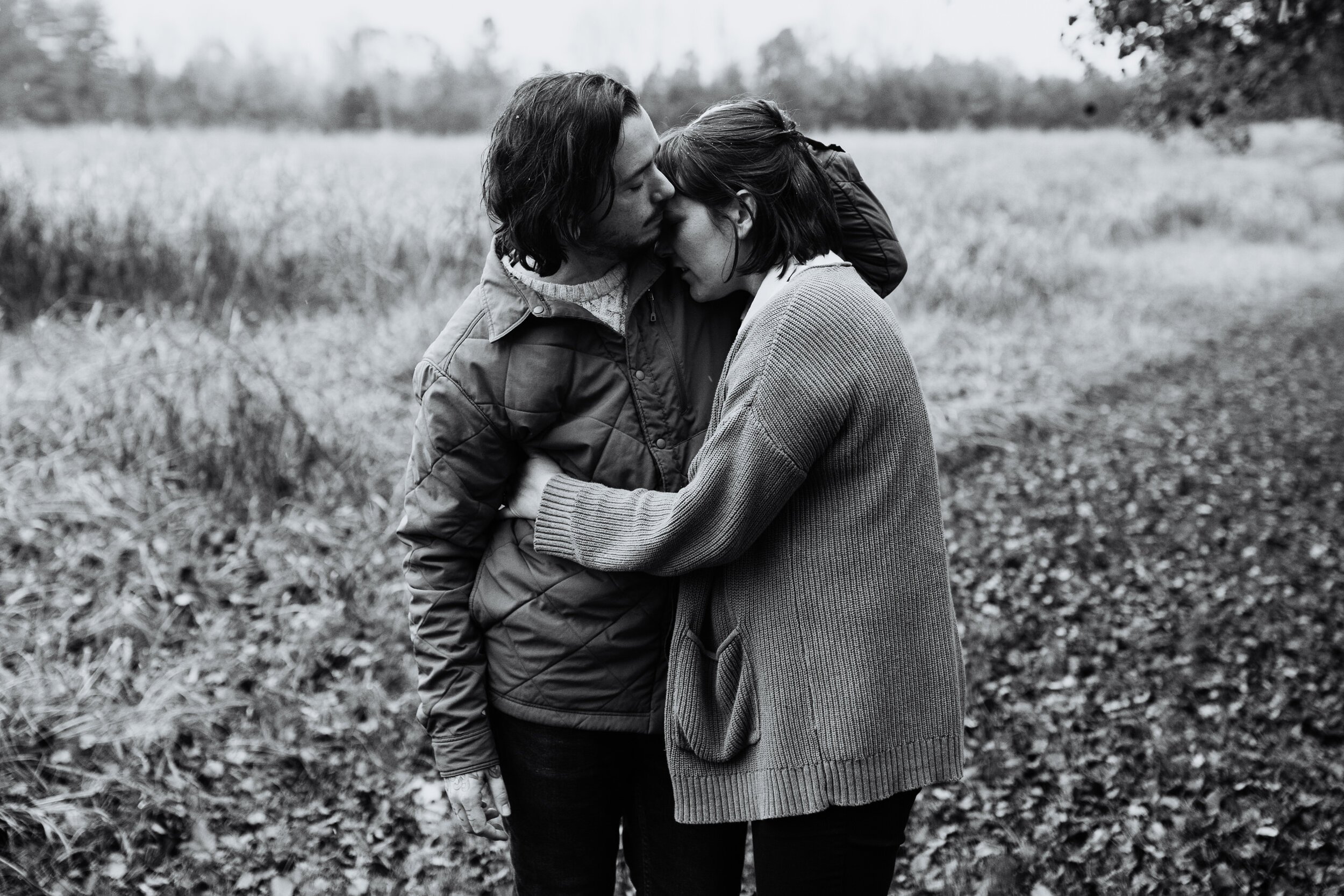 parents hug affectionately while standing in a field black and white 