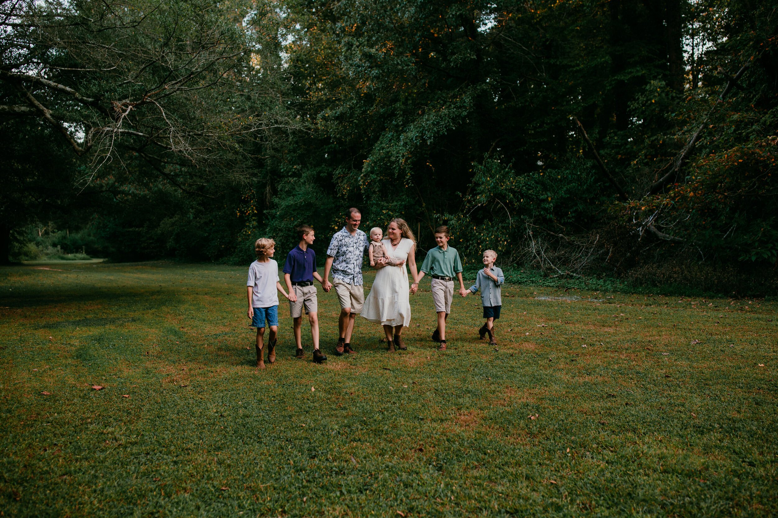 large family walks together hand in hand in green tree lined field