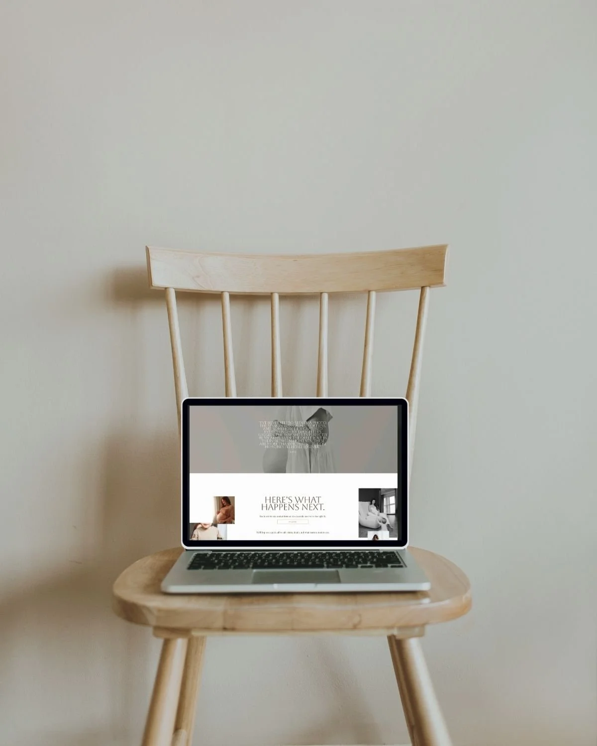 Laptop on a wooden chair in front of a plain wall.