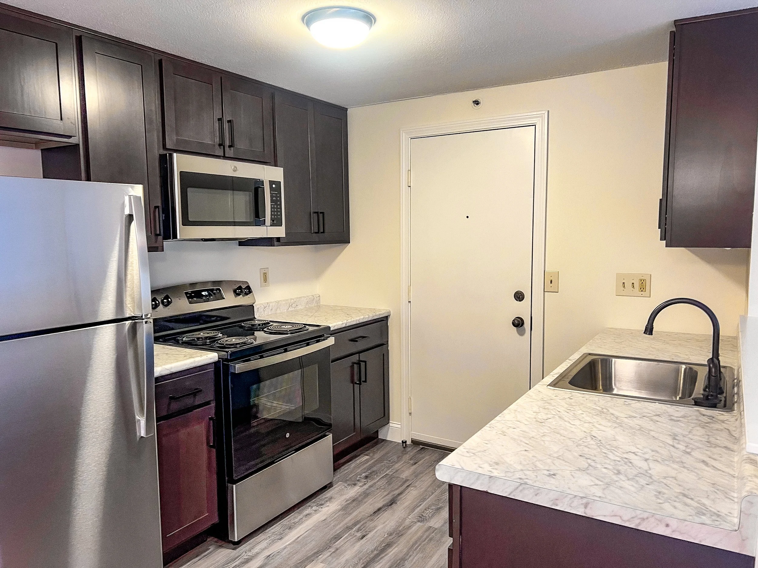Modern kitchen with stainless steel appliances, white marble countertops, dark wood cabinets, and a stainless steel sink.