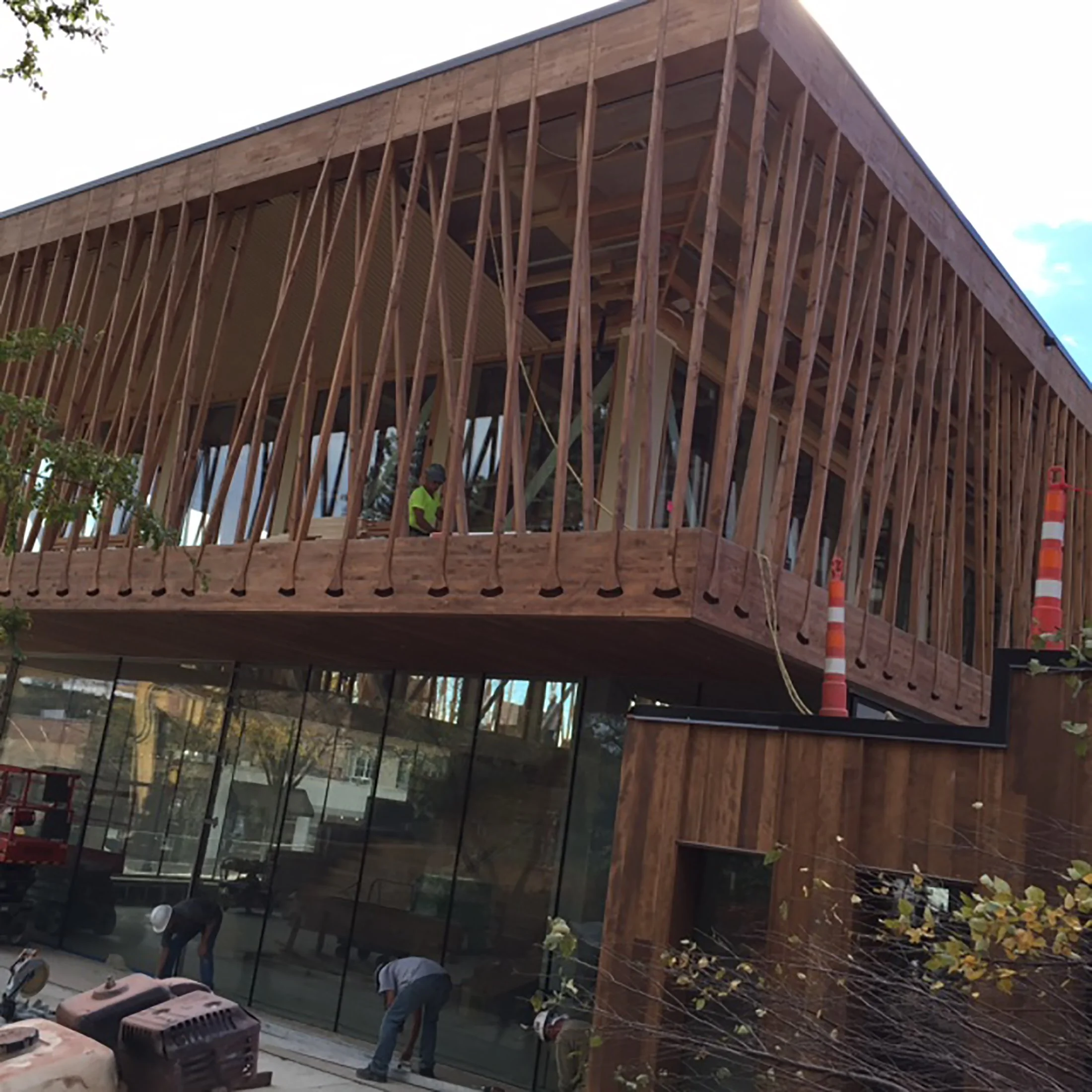 Modern wooden building under construction with workers and safety cones