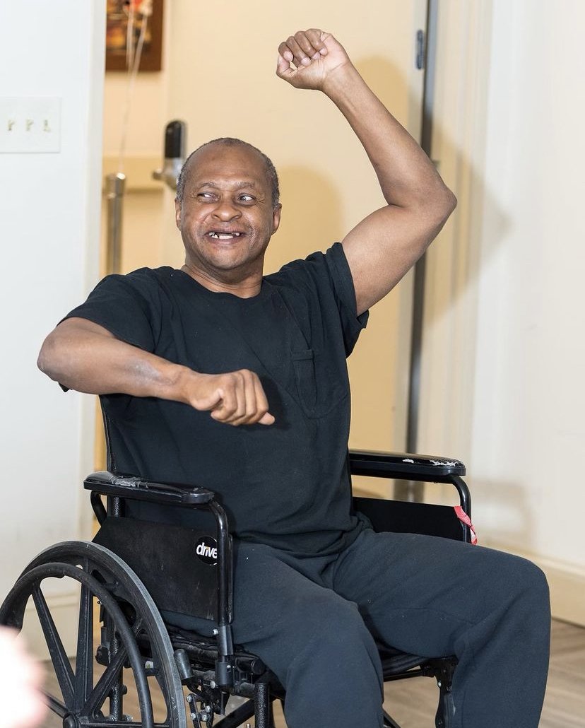 Man in a wheelchair smiling and raising his arm in a celebratory gesture.
