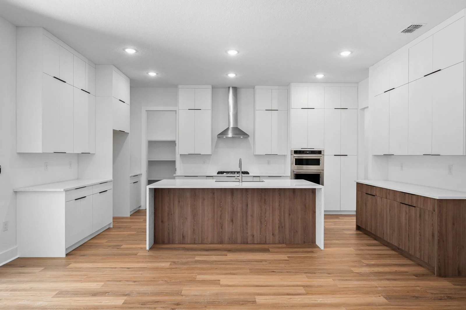 Modern kitchen with white cabinets, a central island with wood paneling, stainless steel range hood, and built-in oven, with wooden flooring.