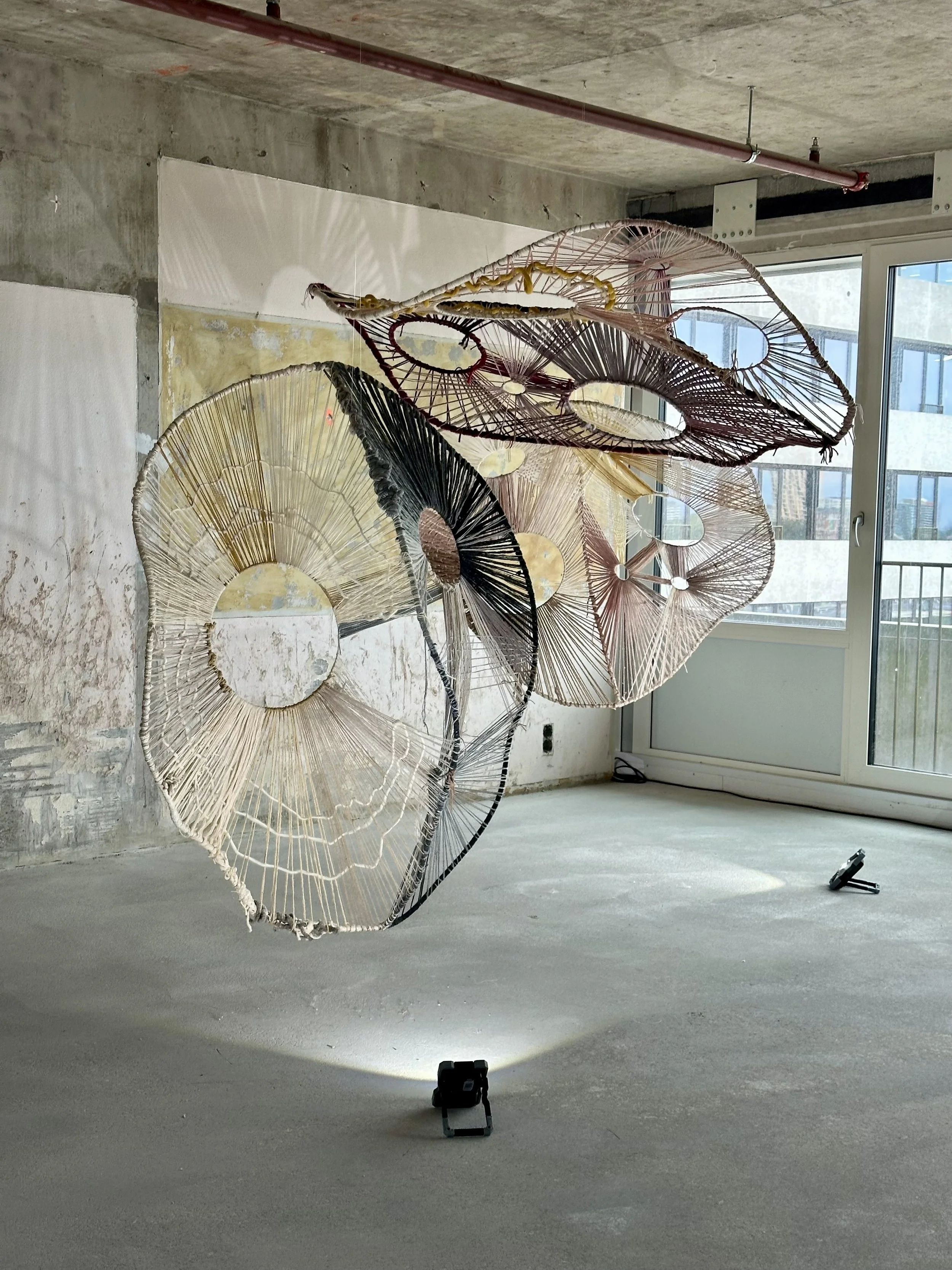 Abstract woven fiber installation in a concrete room with natural light through a window.