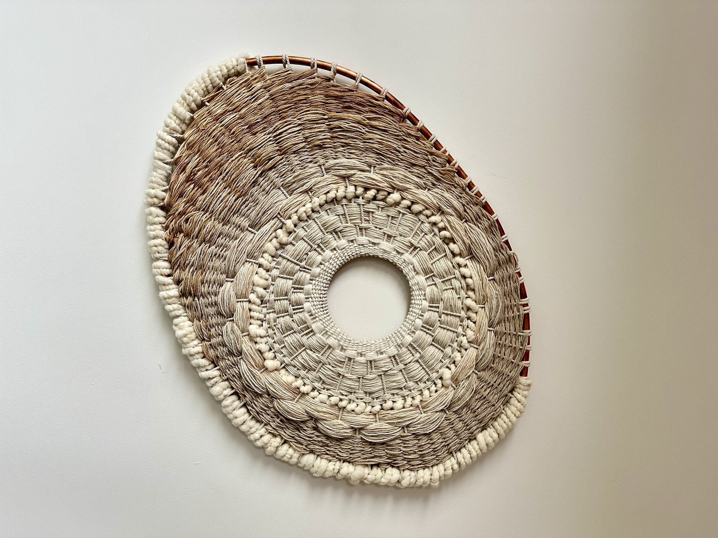 Woven wall hanging with circular and oval shapes on a light background