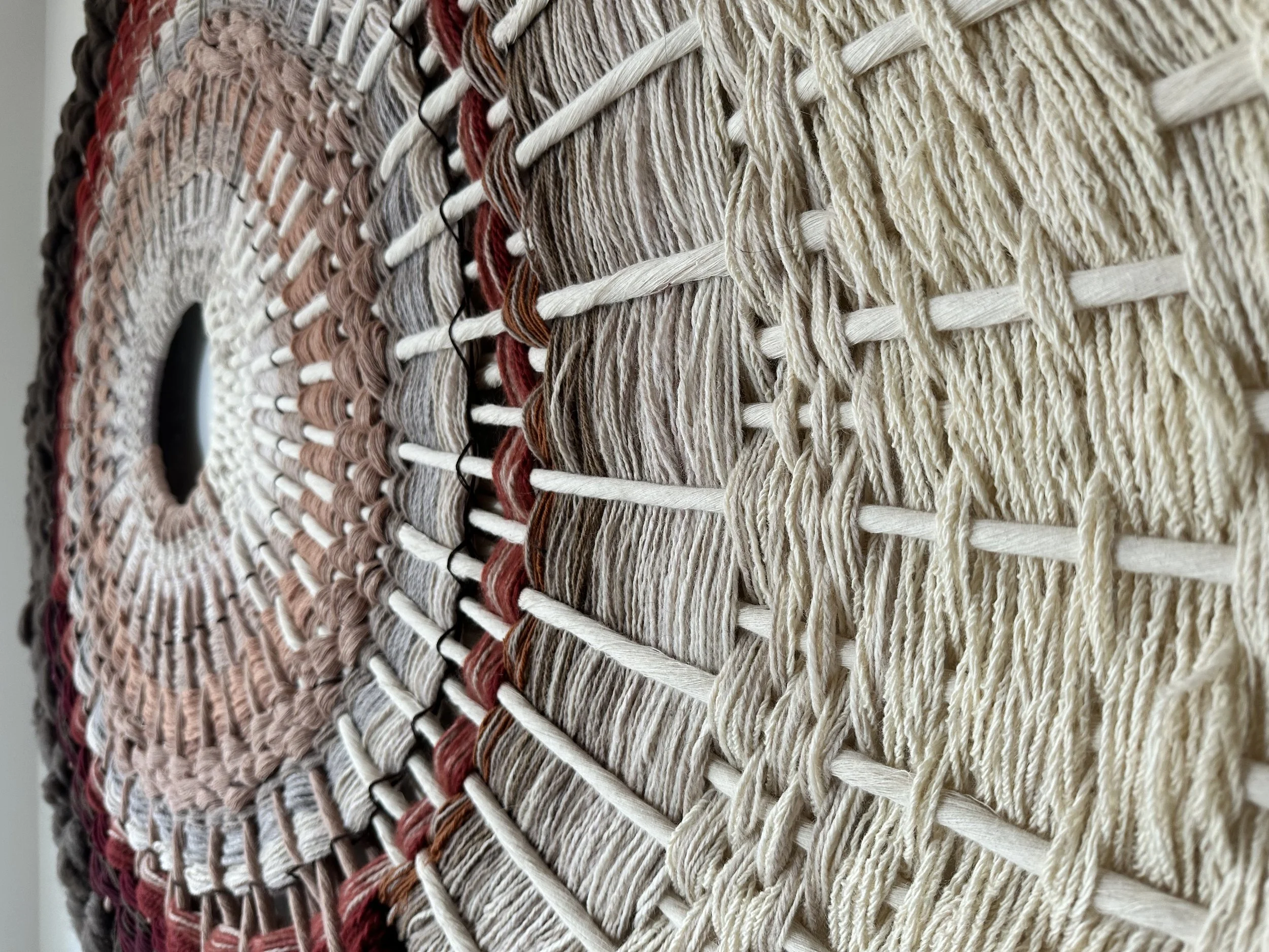Close-up view of a circular woven wall hanging with radial patterns in beige, brown, and cream threads.
