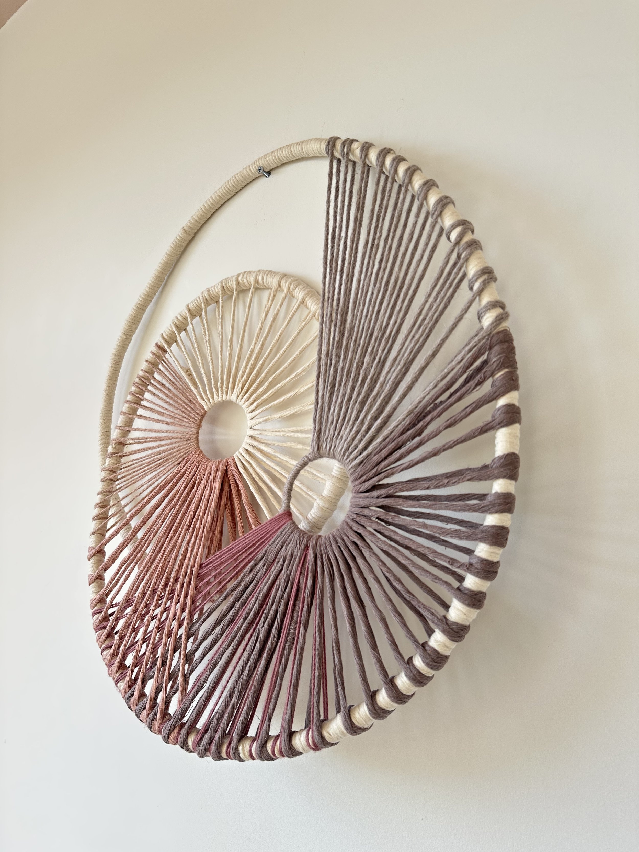 Circular woven wall hanging with beige, brown, and pink yarn