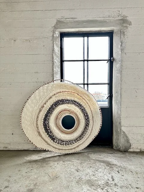A large, decorative woven basket leaning against a window set in a concrete wall.