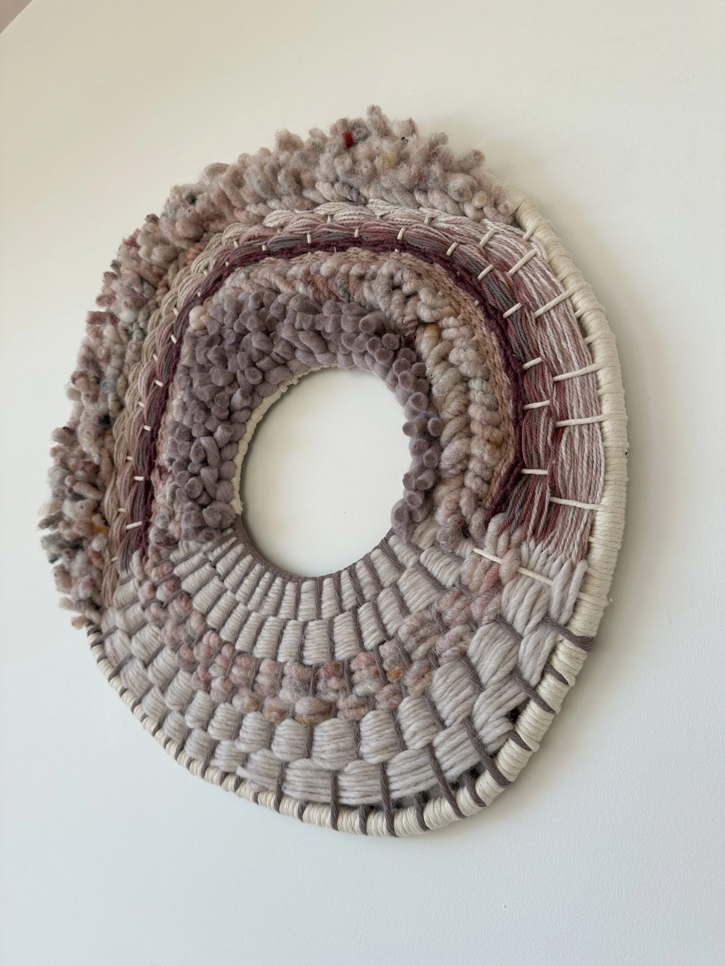 Circular woven textile wall hanging with layered textures and neutral colors
