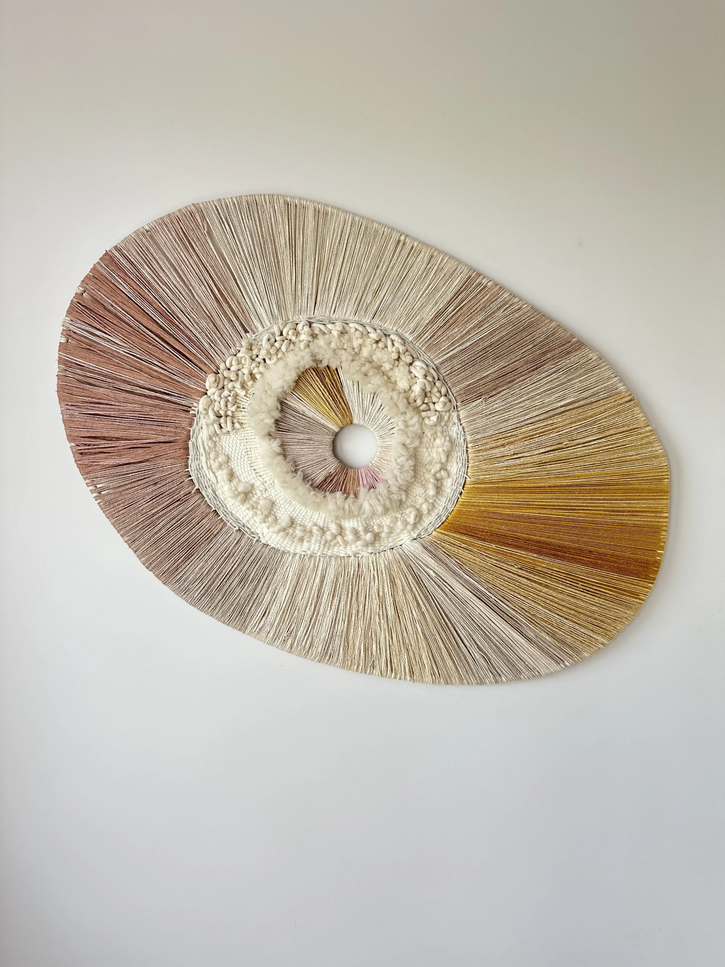 Woven wall hanging with circular design and radial strands in earth tones on white background