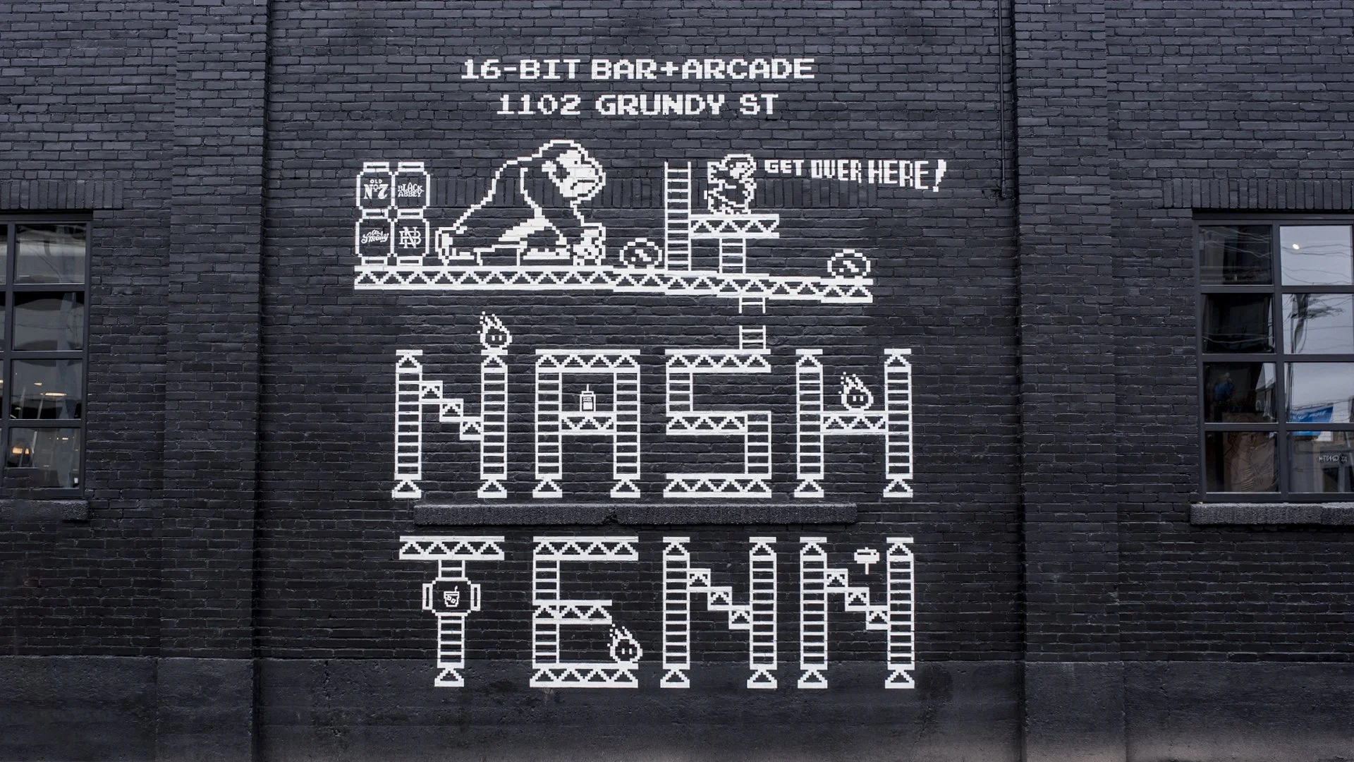 A mural on a brick wall designed in pixel art style, featuring a monkey on a platform with cans, and the words 'Game Over' with a ladder and pixelated characters underneath.