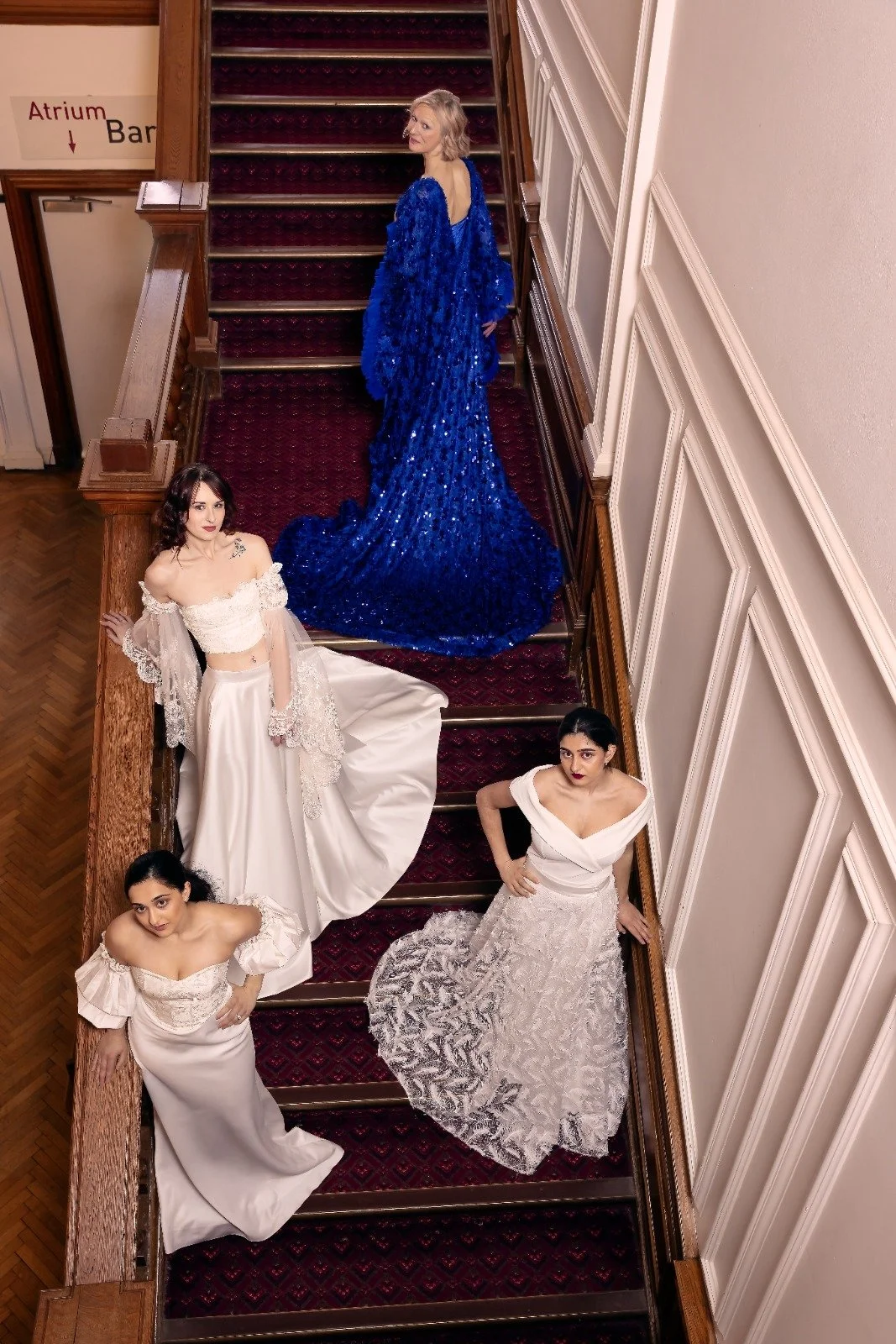 Five women posing on a staircase in formal evening gowns, with elaborate detailing in white and blue.