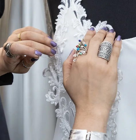 Close-up of a person's hand with multiple rings, adjusting white lace on a black fabric, possibly a wedding dress.