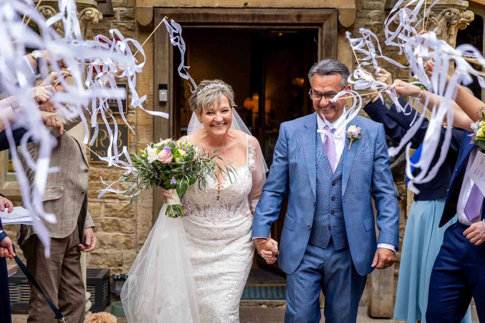 A wedding celebration outdoors with a bride and groom holding hands, surrounded by friends and family, with bubbles floating in the air.