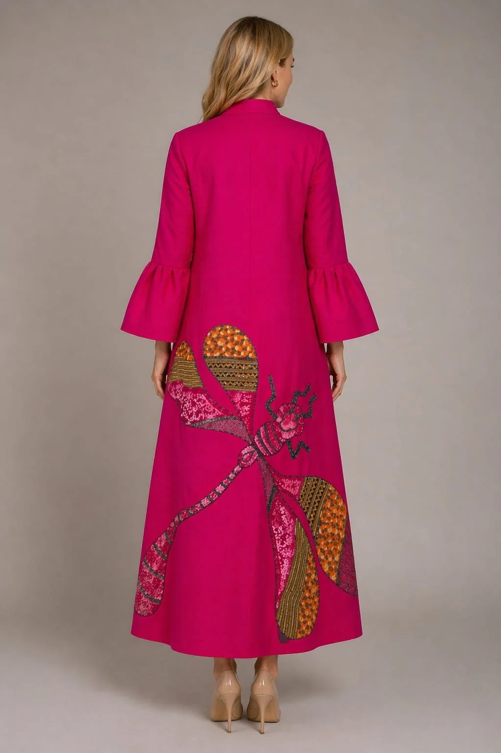 Back view of a woman in a long pink coat with bell sleeves, featuring a large embroidered butterfly design on the lower back.