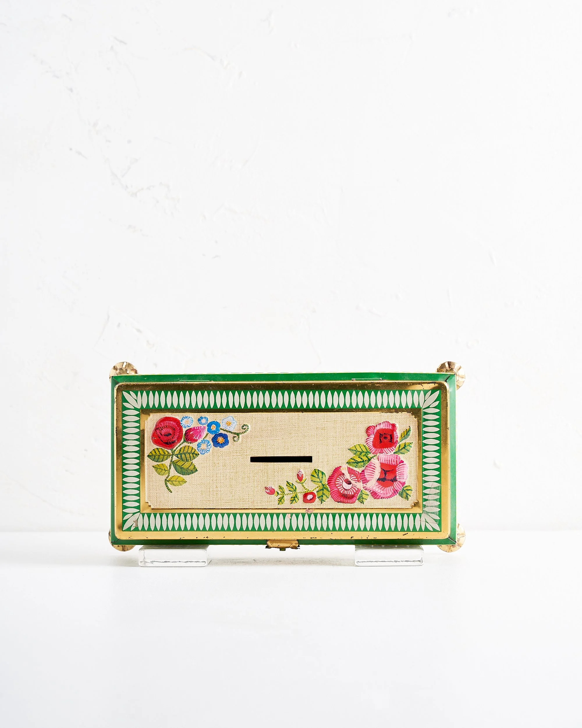 Decorative green painted metal vintage coin bank with floral design on a white surface against a white background.