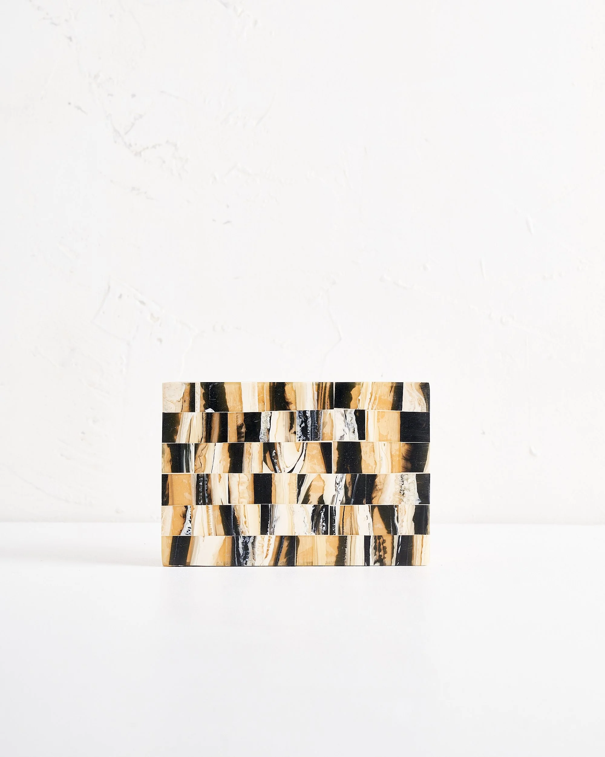 A rectangular object with an alternating pattern of black, beige, and white marble tiles, placed on a white surface against a white textured wall.
