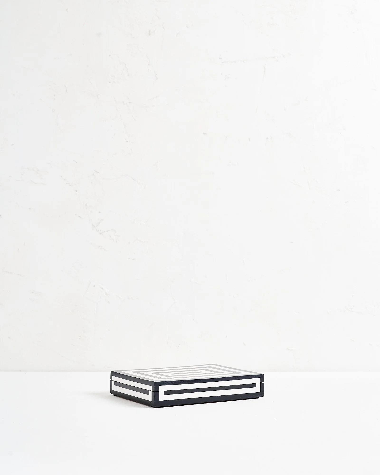 A shallow black and white geometric patterned jewelry box on a white surface against a plain white wall.