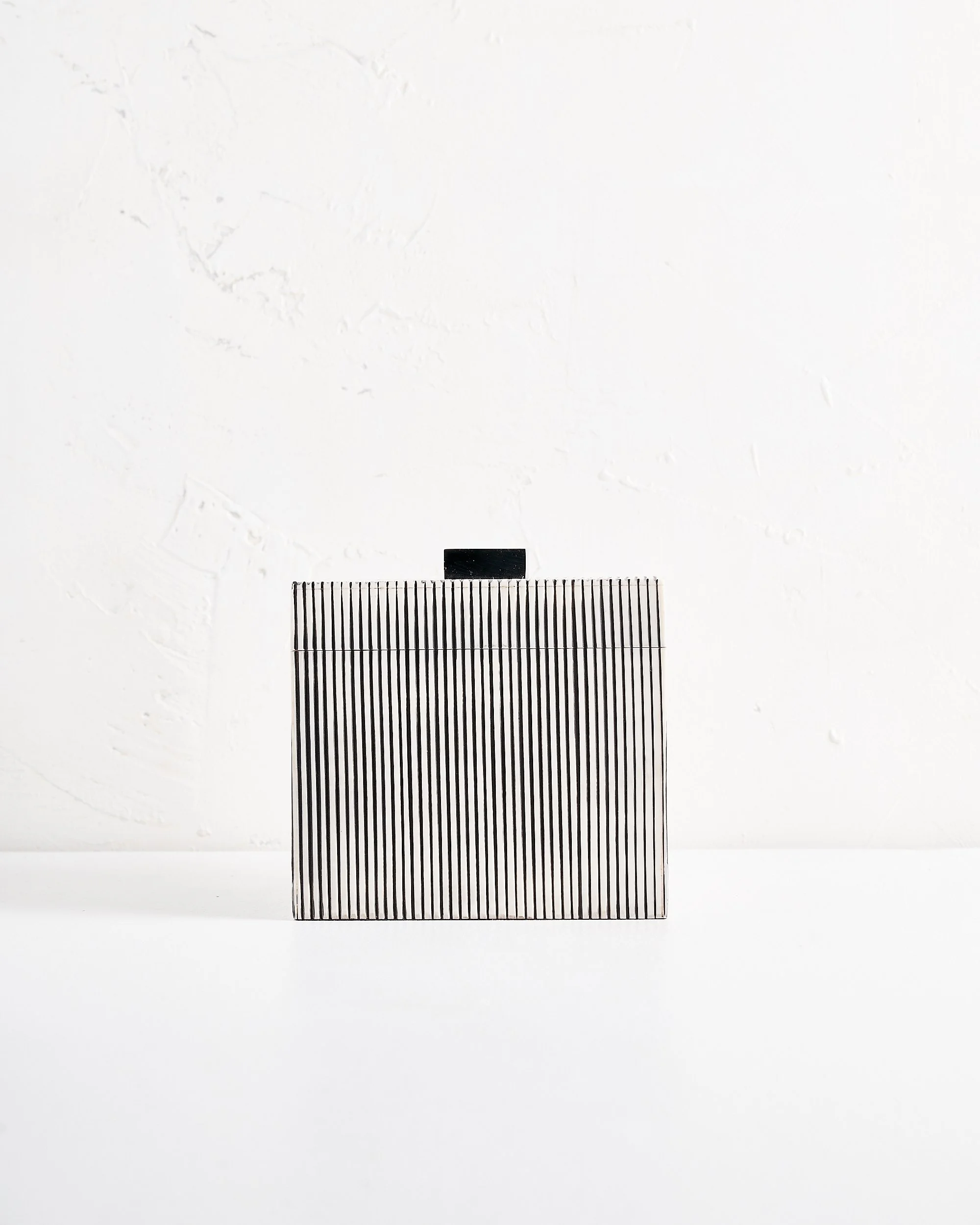 A large modern black and white striped box with a black handle, placed on a white surface against a white wall.