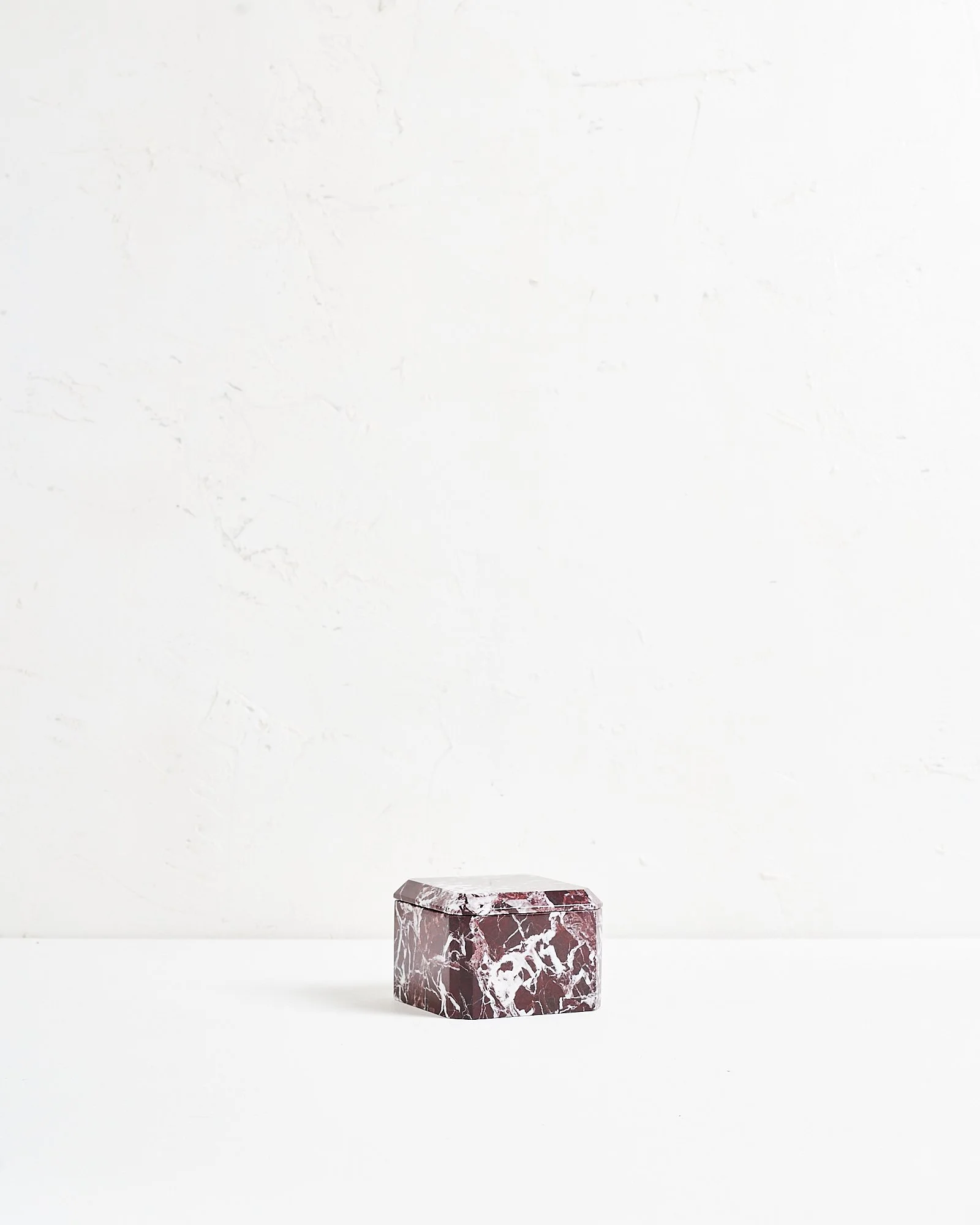 A small, purple and white marble jewelry box on a white surface against a white wall.
