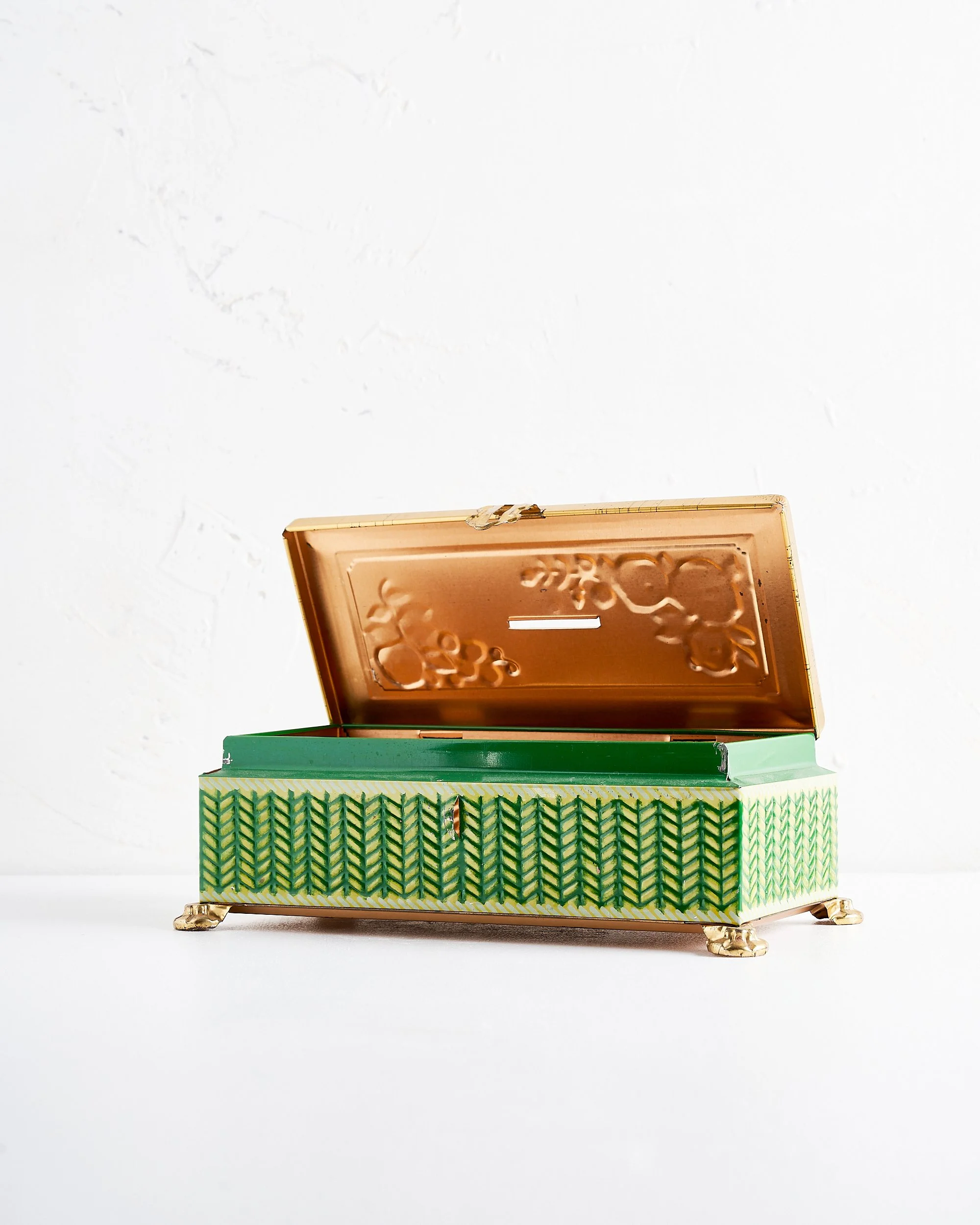 A decorative metal box with a hinged lid, gold accents, and a green and yellow geometric pattern on the exterior, sitting on a white surface with a plain white background.