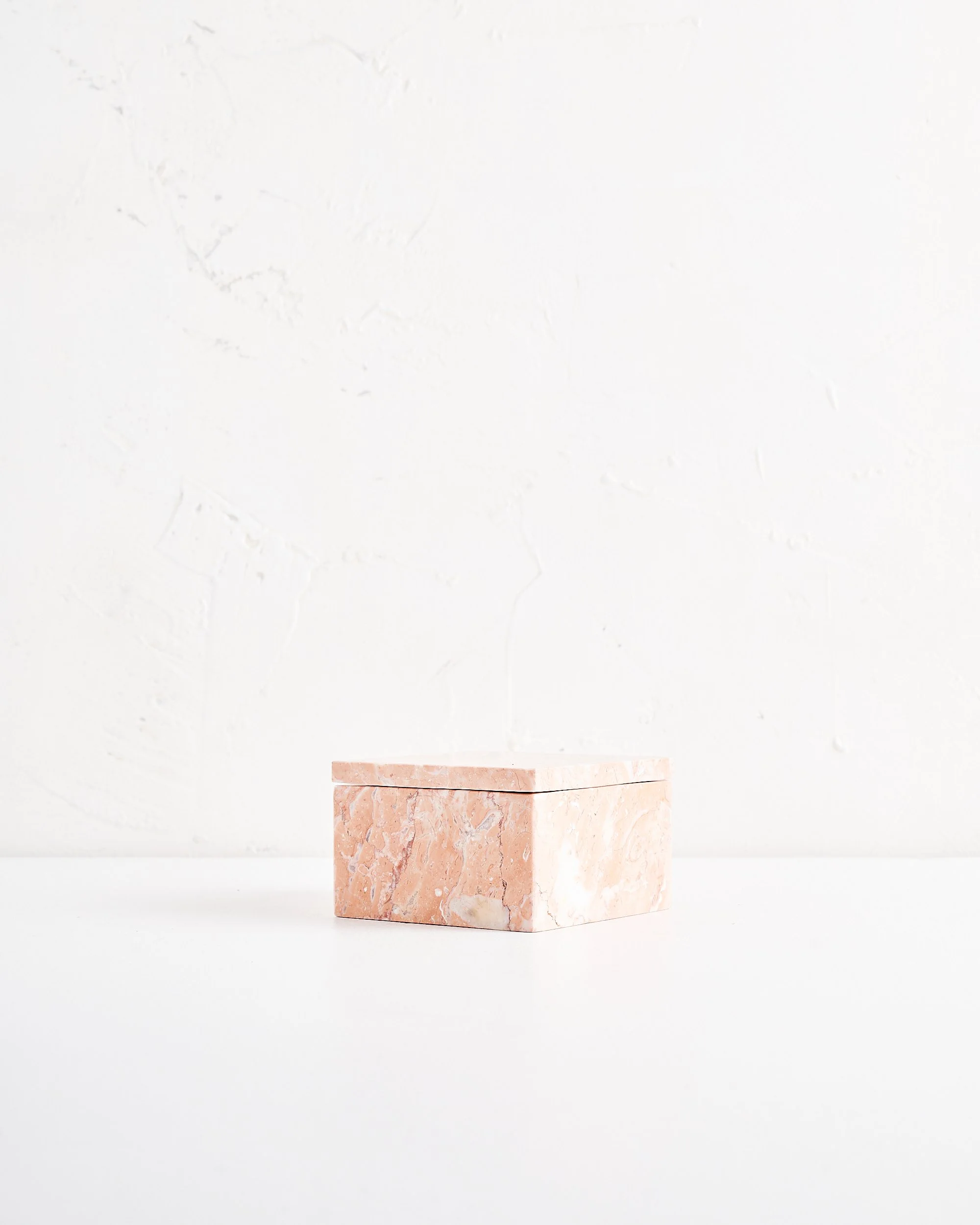 Pink marble rectangular box on white surface with textured white wall background.