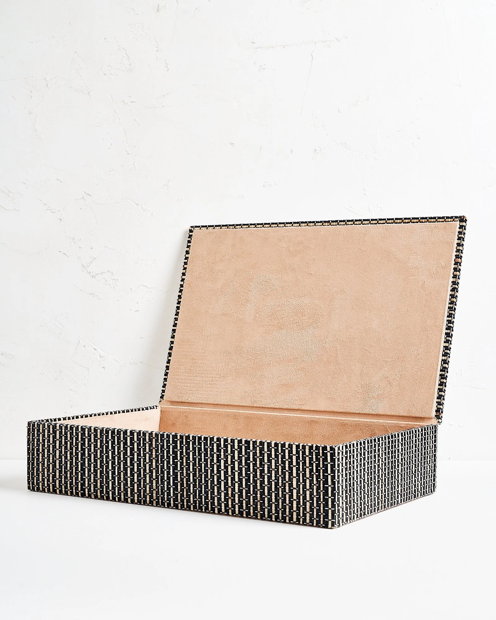 A large decorative rectangular woven black and white patterned storage box with open lid revealing beige fabric interior against a white textured wall.