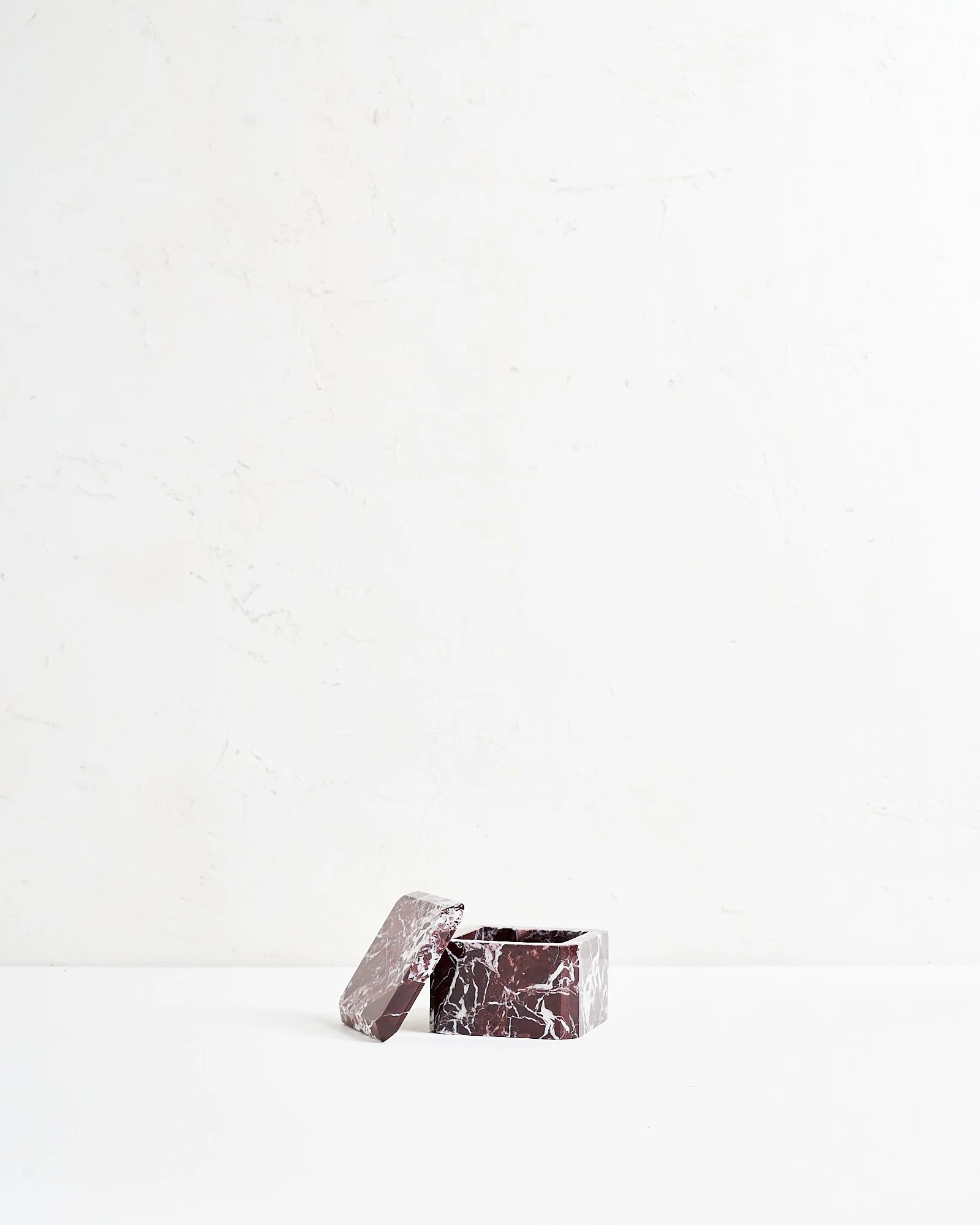 A small, purple and white marble jewelry box with a lid leaning on side, placed on a white surface against a plain white background.