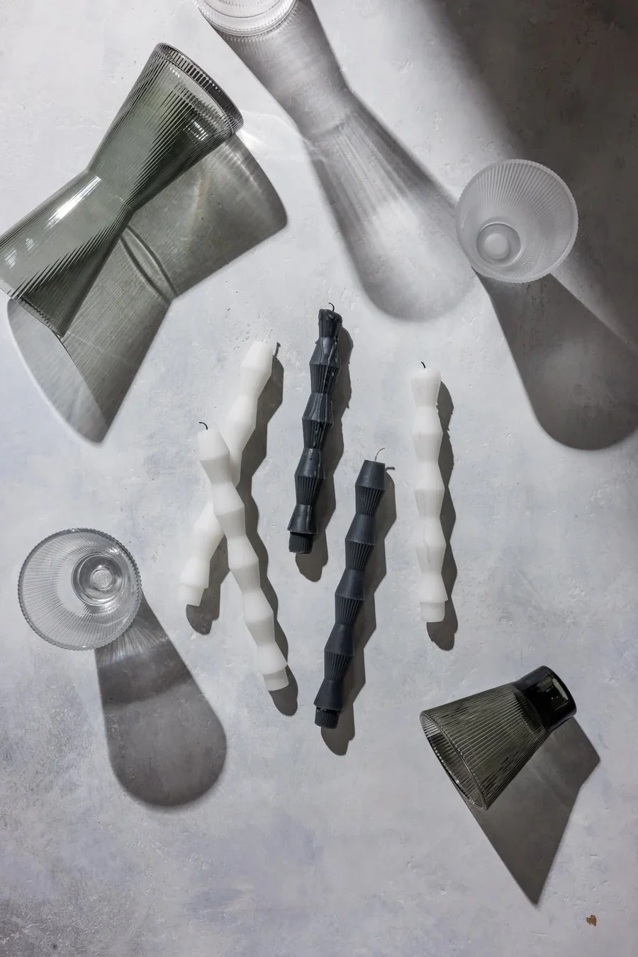 Arrangement of glassware and geometric candles on a textured surface casting shadows