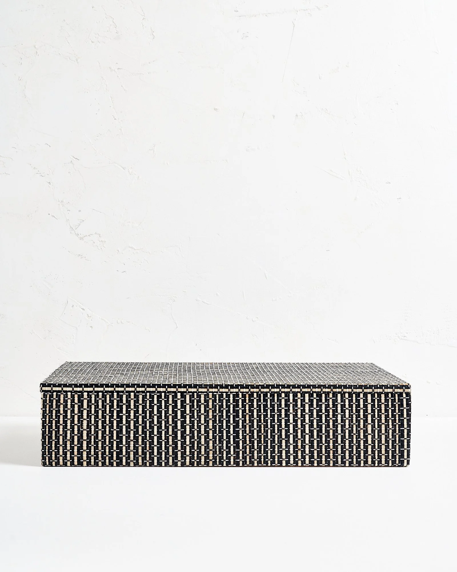 A large decorative rectangular woven black and white patterned storage box or against a white textured wall.