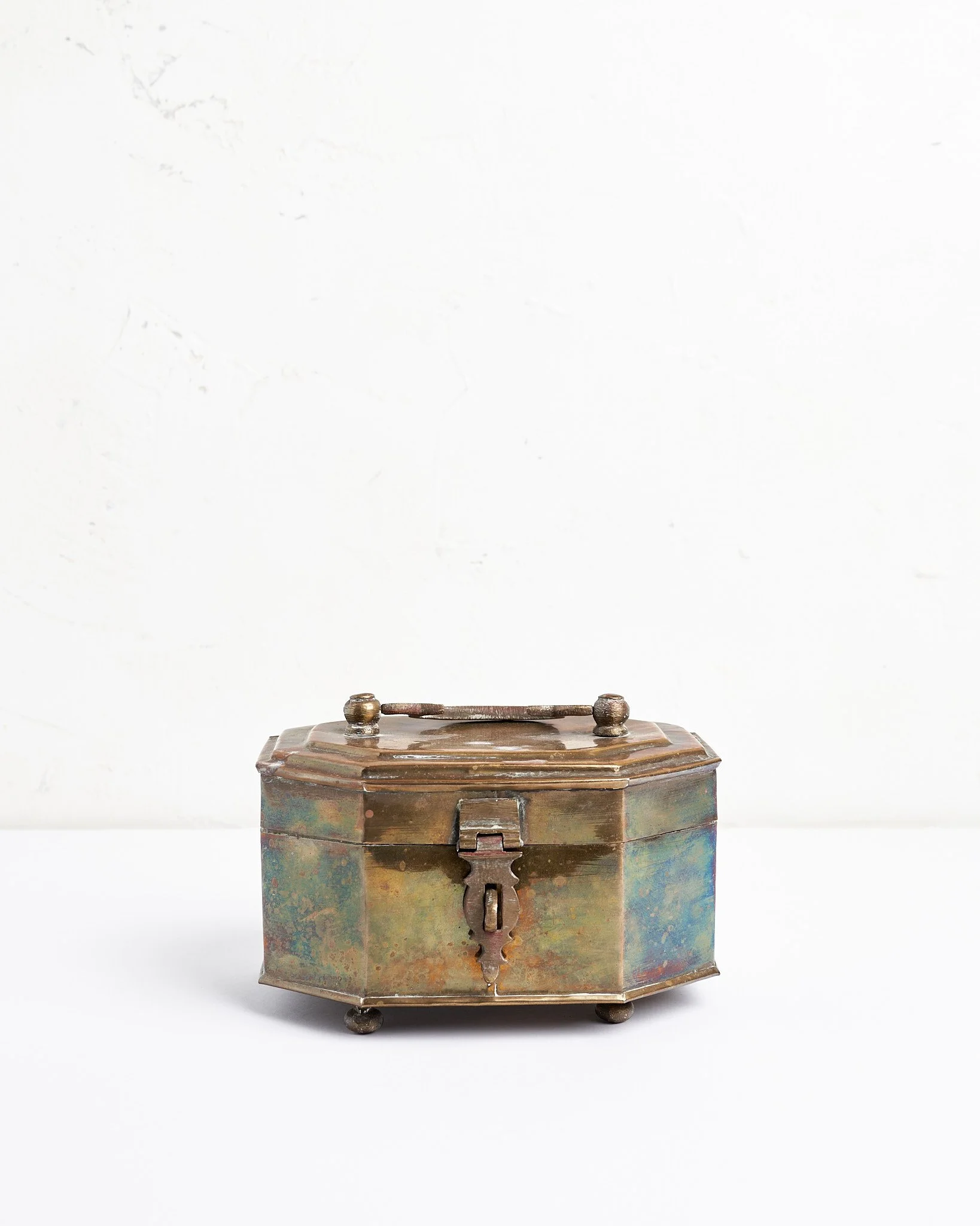 An ornate, vintage metal box with a lock, sitting on a white surface against a plain white background.