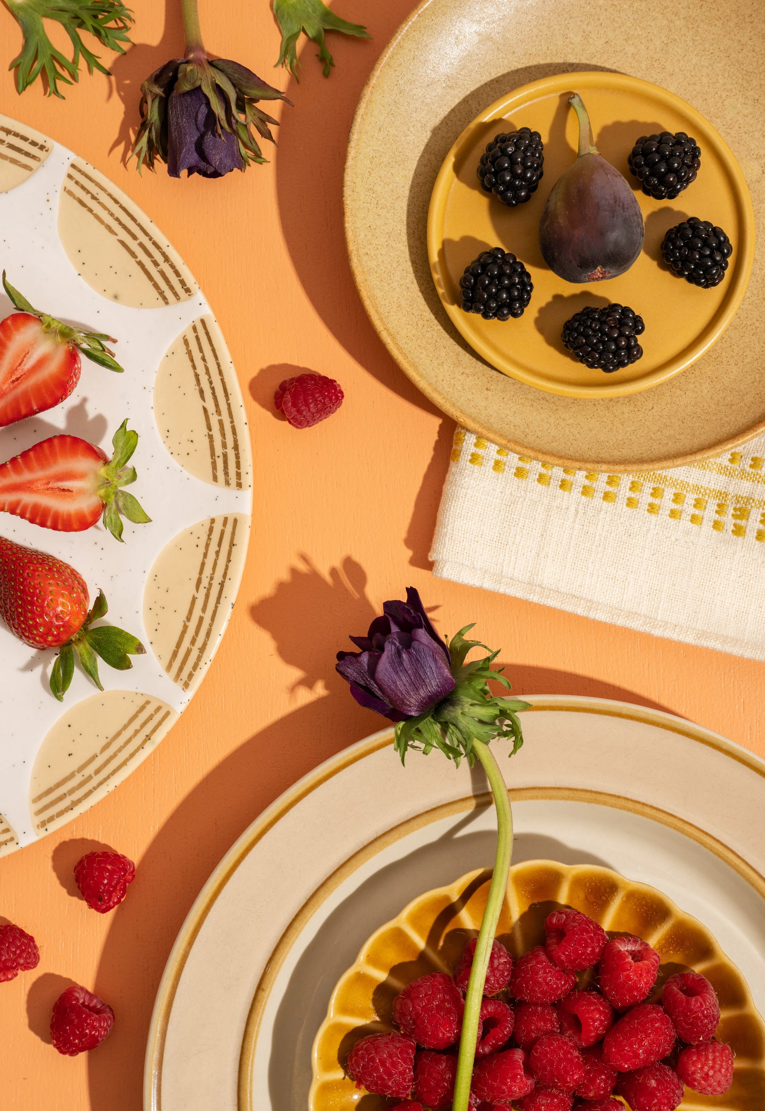 Assorted fresh berries including raspberries, blackberries, and strawberries on ceramic plates with floral decorations on a peach background.