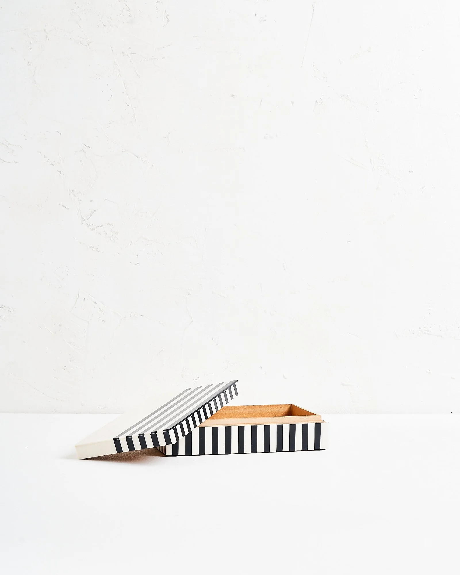 An open modern rectangular jewelry box with black and white verticalstriped pattern, lid leaning on side with horizontal black and white stripes, on a white surface against a plain white wall.