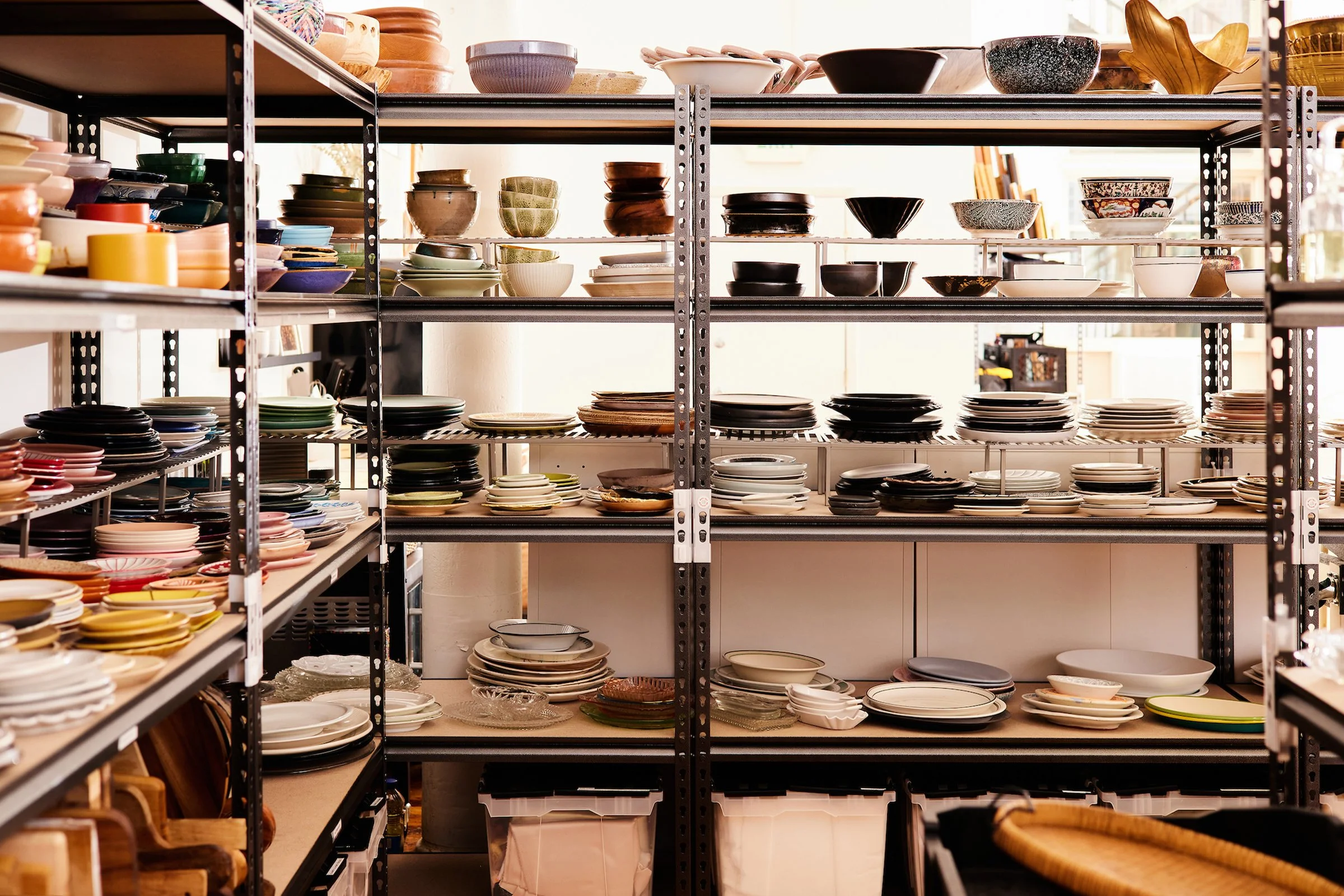 Shelves filled with assorted bowls and plates in various colors and styles at prop up shop's studio.