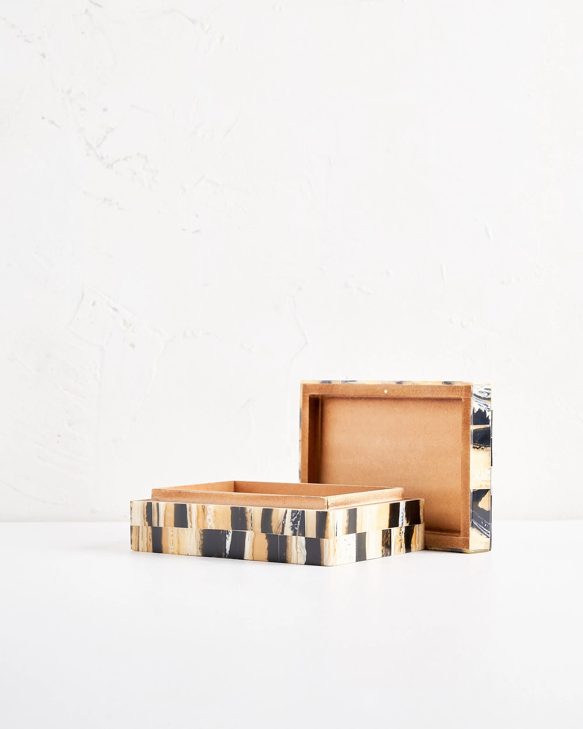 An open decorative box with black, beige, and white marble pattern on a white surface against a textured white wall.